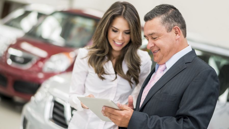 two people smiling looking at a tablet in a car dealeship